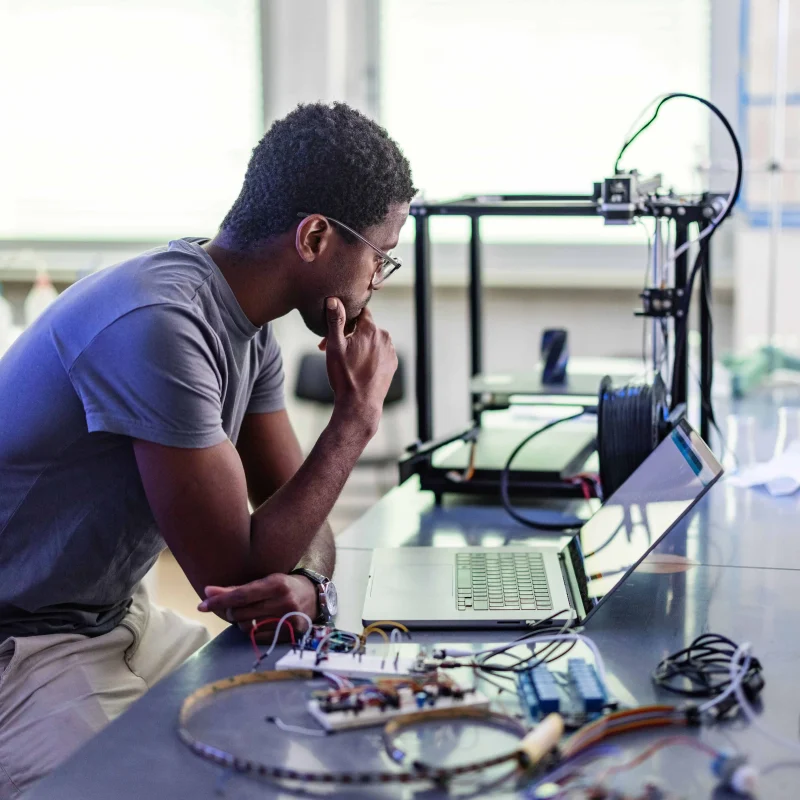 Young man technician sitting in the chair, thinking and repairing his 3D printer in the laboratory
